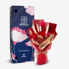 Red preserved rose bouquet with wheat stalks and dried flowers in red mesh wrapping, next to a dark blue box with pink floral designs.