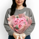 Woman holding a pink spray rose and eucalyptus bouquet with a cream ribbon.