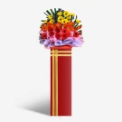 A vibrant flower arrangement of gerbera daisies in red, orange, and yellow sits atop a red pedestal with gold trim.
