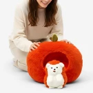 A woman kneels beside an apple-shaped plush bed for a hedgehog toy.