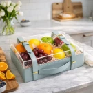Fruit gift box with grapes, apples, oranges, and lemons on a kitchen counter.