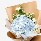Blue hydrangea bouquet with white carnations and asters, wrapped in brown paper.