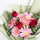 Bouquet of red roses, pink gerberas, and pink carnations with eucalyptus leaves, wrapped in pale green paper.