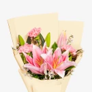 A bouquet of pink lilies and carnations in pale yellow paper wrapping.