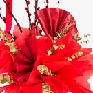 A red flower arrangement in a basket with red paper, gold leaves, and red branches.