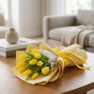A bouquet of 10 bright yellow tulips with green leaves, wrapped in cream and yellow paper, tied with a yellow ribbon.