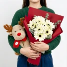 Person in green sweater holding white gerbera daisies and a plush reindeer with red scarf.