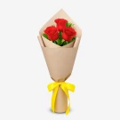 Three red roses with rosal leaves in a brown paper wrap, tied with a yellow ribbon.