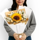 Woman in grey hoodie holding "Bask in Sweetness" bouquet featuring a sunflower and chocolates.