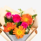 Bright bouquet of orange gerbera daisies and pink roses in tan paper wrapping.