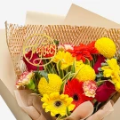 Bright bouquet of red, yellow, and orange flowers with a gold "Thank you" topper.