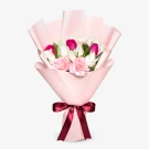 Pink and white roses and pink carnations arranged in a soft pink paper bouquet, tied with a burgundy ribbon.