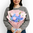 Pink roses and blue hydrangeas with eucalyptus in pink and white paper, tied with a blue ribbon.
