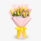 Bouquet of pink and yellow tulips wrapped in light pink paper, tied with a yellow ribbon.