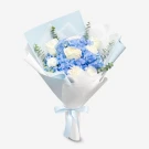 Blue hydrangea and white rose bouquet with eucalyptus, wrapped in blue paper and tied with a blue ribbon.