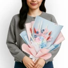 Woman holding a bouquet of pastel pink, blue, and white preserved flowers with dried accents.