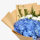 Blue hydrangea bouquet with white carnations and asters, wrapped in brown paper.