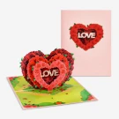 Pop-up heart card with red roses and the word "LOVE" inside, on a green, grassy background.