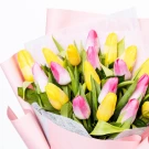 A bouquet of pink and yellow tulips, wrapped in pale pink paper.