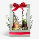 Festive miniature Christmas village scene inside a gift box with red ribbon.