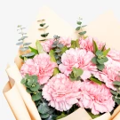 Pink carnations and eucalyptus leaves in a light peach bouquet wrap.