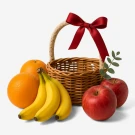 Fruit basket with bananas, oranges, red apples, and a red ribbon bow.