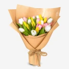 A bouquet of 30 assorted tulips in pink, white, and yellow, wrapped in brown paper and tied with twine.