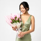 Pink tulips bouquet wrapped in pink and white paper with a white ribbon.