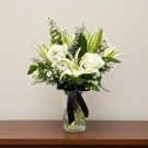 White lilies, roses, and matthiola in a glass vase with a black ribbon.