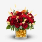 Christmas flower arrangement with red roses, candy canes, ornaments, and a candle in a glass vase.