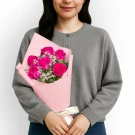 Person holding a bouquet of 6 bright pink roses wrapped in pink paper, tied with a cream ribbon.