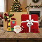 Christmas gift box with red blanket, Santa mug, Dilmah tea, and honey on a wooden table.