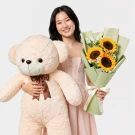 Woman smiling, holding a giant teddy bear and sunflowers.