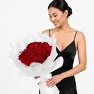 Woman in gray sweater holding a large bouquet of 30 red roses wrapped in white paper.