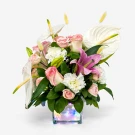A floral arrangement in a clear cube vase with fairy lights, featuring pink roses, white lilies, and white calla lilies.