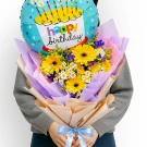 A bouquet of yellow gerbera daisies and white daisies with a blue happy birthday balloon.