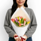 Woman in gray sweater holding a bouquet of colorful tulips wrapped in white paper, tied with a ribbon.