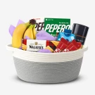 Gift basket overflowing with snacks including bananas, cookies, crackers, candy bars, and a coffee tin.