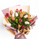 Bouquet of red, white, and orange tulips with greenery, wrapped in pastel paper and tied with a ribbon.
