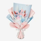 Bouquet of pink and blue preserved flowers with dried wheat and foliage, wrapped in light blue and pink paper, tied with a white ribbon.