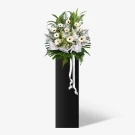 White gerberas and greenery arrangement on a black stand with white ribbons.