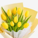 Bouquet of ten bright yellow tulips with green leaves, wrapped in yellow and cream paper.