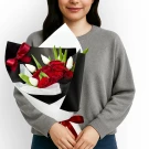 Woman in grey sweater holding a bouquet of red roses and white tulips, tied with red ribbon.