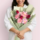 Woman holding a bouquet of pink gerberas, pink carnations, and red roses, wrapped in green paper.