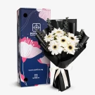 White gerbera daisies with eucalyptus in black paper, next to a blue box with floral designs.