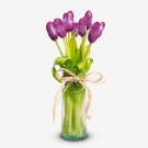 A vase filled with 10 violet tulips tied with a light pink ribbon.