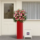 Pink Jubilee flower arrangement on a red stand, in front of a door and window.