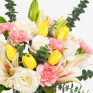 Bouquet of white roses, pink carnations, yellow tulips, and white lilies with eucalyptus leaves.