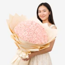 Woman holding a very large bouquet of 99 light pink roses, wrapped in neutral paper.