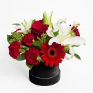 Round black box with red carnations, roses, gerbera, and white lilies.